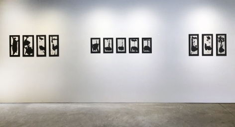 Twelve black ink drawings by Richard Stankiewicz on white paper mounted on black matts hanging on a white wall