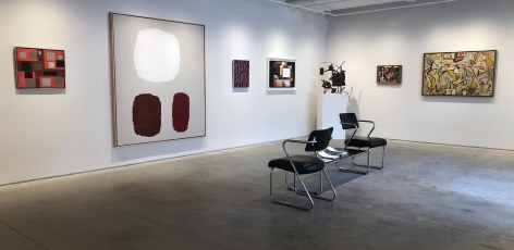 Six paintings and a sculpture installed in the Washburn Gallery.  Two black chairs and table positioned in the middle of the room.